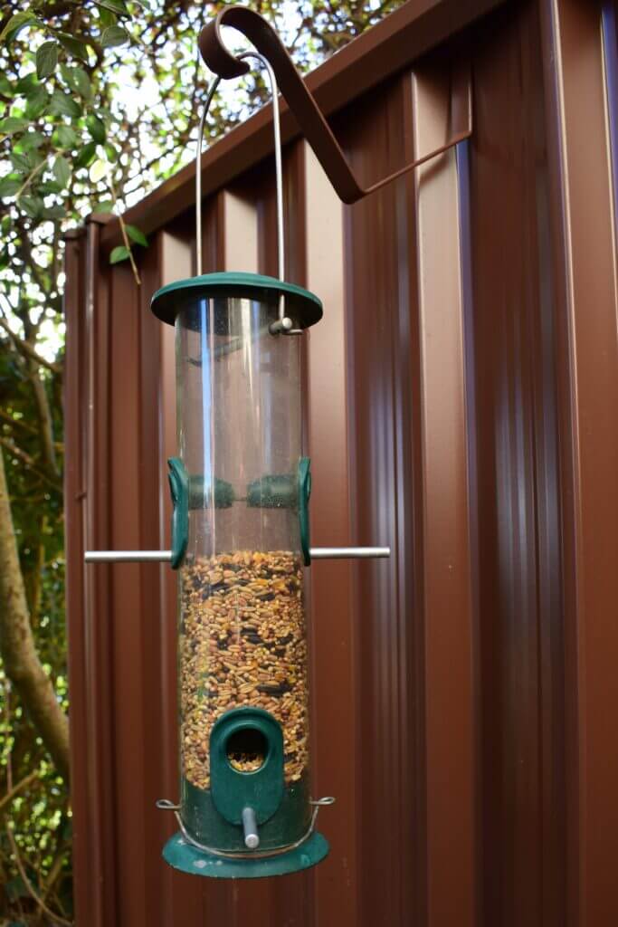 hanging bird feeder against brown colourfence 