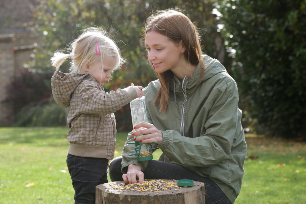 Parent and child filling a wild bird feeder